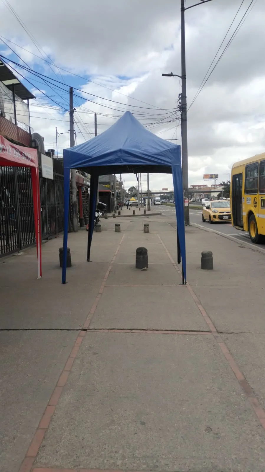 Carpa plegable azul de cuatro patas instalada sobre el andén de una avenida en Bogotá