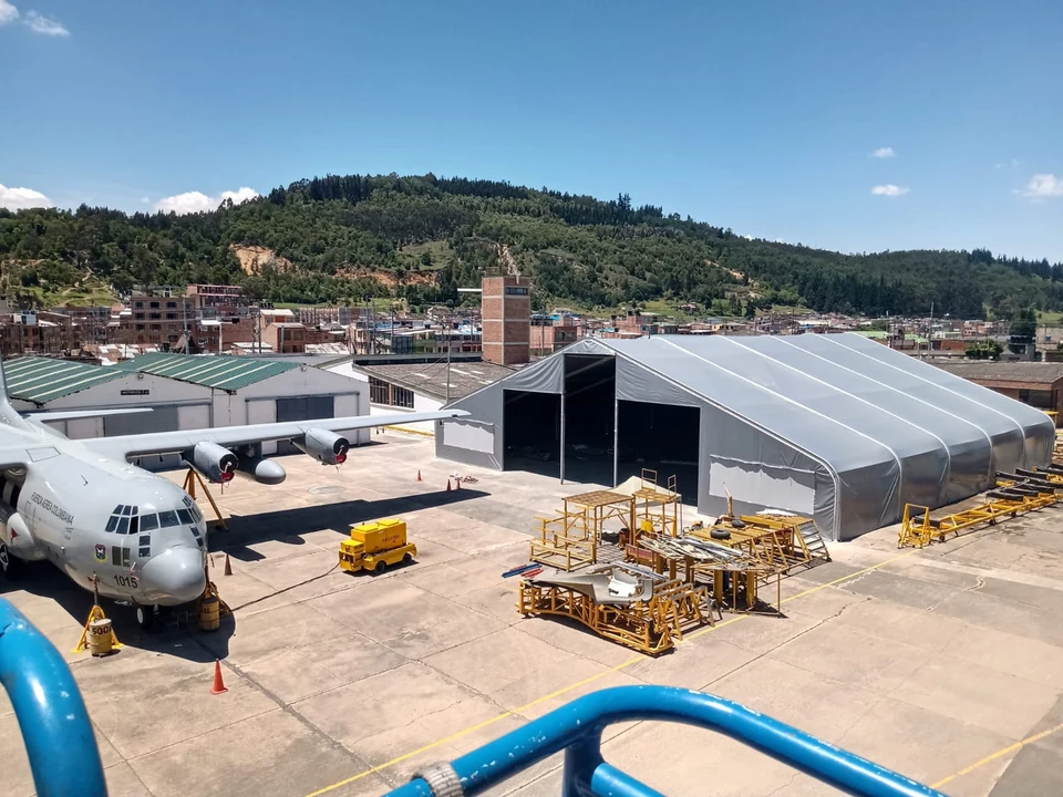 Hangar de estructura textil de gran luz con techo gris a dos aguas y portón frontal abierto de toda la altura, instalado sobre la plataforma de un aeropuerto, con una aeronave de transporte estacionada al lado
