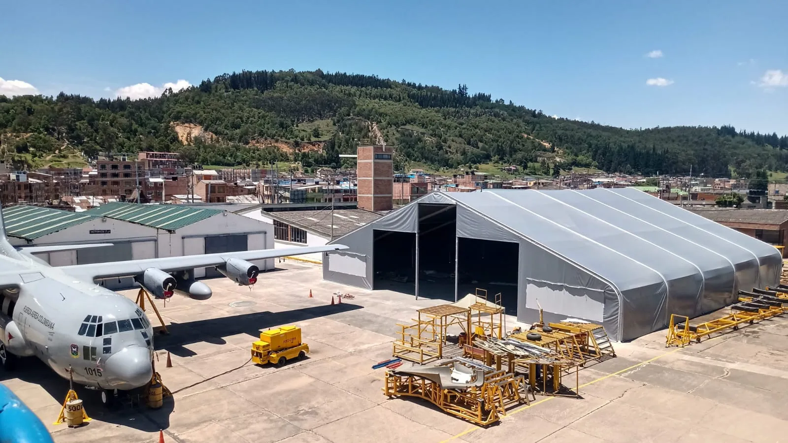 Hangar de estructura textil de gran luz construido por Carpas Cubricol sobre la plataforma de un aeropuerto, con el portón frontal abierto de toda la altura y una aeronave de transporte estacionada al lado