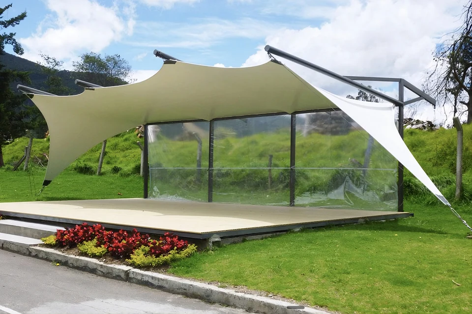 Techo de membrana tensada sobre una plataforma de madera al aire libre, con cerramiento lateral transparente y estructura metálica oscura
