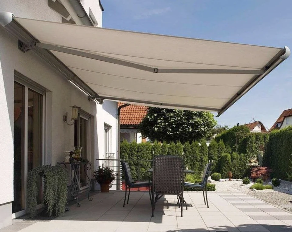 Parasol retráctil de brazos articulados completamente extendido sobre la terraza de una casa, con la lona clara cubriendo la zona de comedor